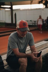 man wearing crew-neck t-shirt using smartphone while sitting on brown wooden bench